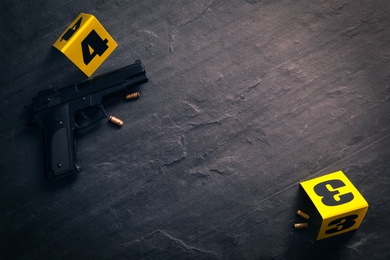 Bullets, gun and crime scene markers on black slate background, flat lay. Space for text