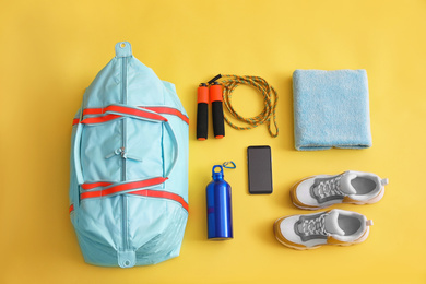 Gym bag, smartphone and sports equipment on yellow background, flat lay