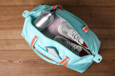 Open sports bag full of gym stuff on wooden background, top view