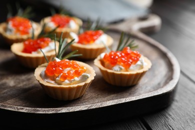 Photo of Delicious tartlets with red caviar and cream cheese served on wooden table, closeup
