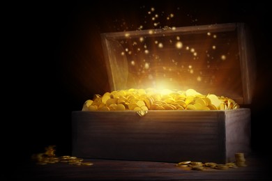 Open treasure chest with gold coins on wooden table against black background