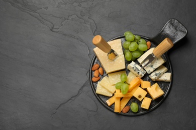 Cheese platter with specialized knife and fork on black table, top view. Space for text