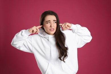 Emotional young woman covering ears with fingers on pink background