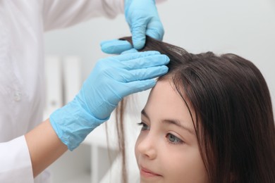 Doctor examining little girl's hair indoors. Anti lice treatment