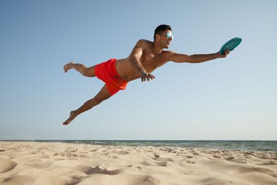 Sportive man jumping and catching flying disk at beach
