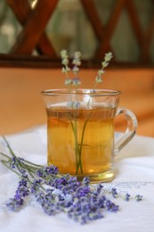 Photo of Tasty herbal tea and fresh lavender flowers on white fabric