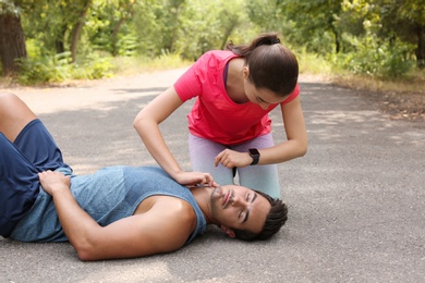 Young woman checking pulse of unconscious man in park. Space for text