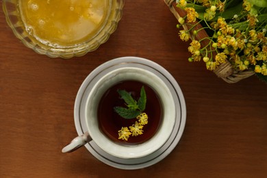 Cup of hot aromatic herbal tea, honey and linden blossoms on wooden table, flat lay