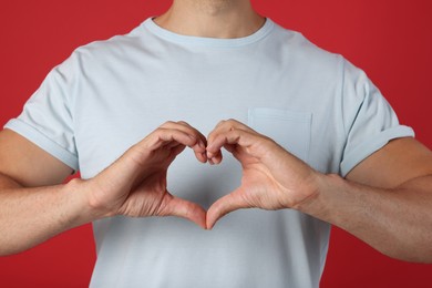 Photo of Man making heart with hands on red background, closeup
