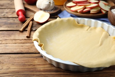 Baking dish with raw dough for apple pie and ingredients on wooden table