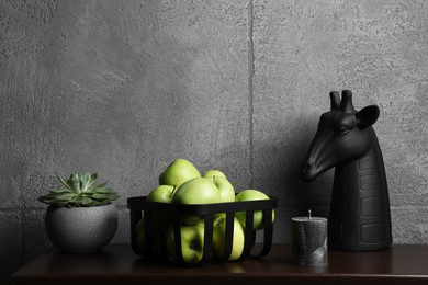 Wooden shelf with potted plant, decorative figure of giraffe and apples against grey wall, space for text