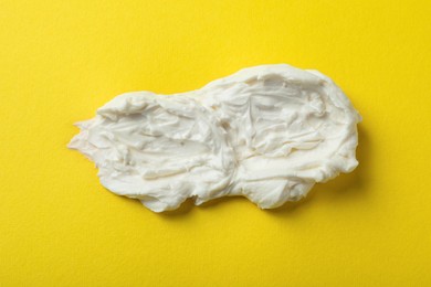 Smear of delicious cream cheese on yellow background, top view