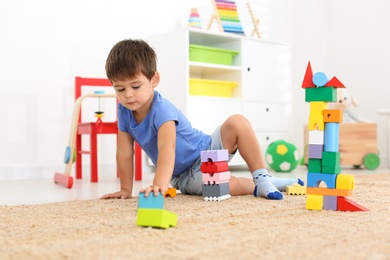 Photo of Cute little boy playing with colorful blocks on floor at home. Educational toy