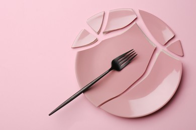 Pieces of broken ceramic plate and fork on pink background, flat lay. Space for text