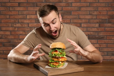 Photo of Young hungry man eating huge burger at table