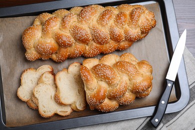 Baking tray with homemade braided bread and knife on wooden table, top view. Traditional Shabbat challah