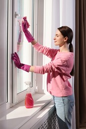 Young woman cleaning window glass with rag at home