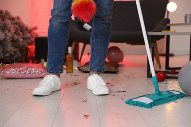 Man with mop cleaning messy room after New Year party, closeup of legs