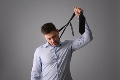 Depressed businessman holding tie like noose against light grey background
