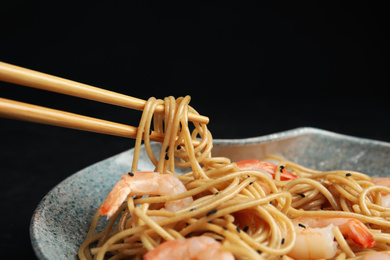 Chopsticks with tasty buckwheat noodles on black background, closeup