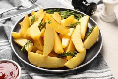 Plate with tasty baked potato wedges and rosemary on white wooden table, closeup