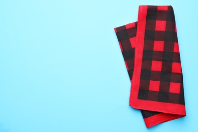 Folded red checkered bandana on light blue background, top view. Space for text