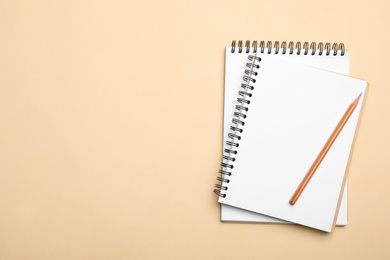 Open notebooks and pencil on beige background, top view. Space for text