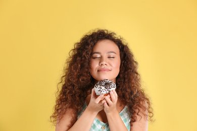 Beautiful African-American woman with donut on yellow background