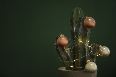 Photo of Beautiful cactus with Christmas balls and festive lights  on green background, closeup. Space for text