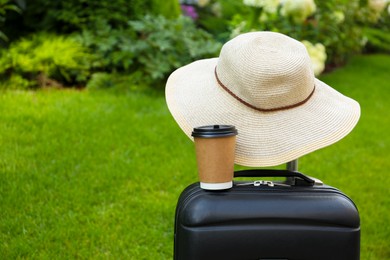 Photo of Paper cup of hot coffee with beige hat on suitcase outdoors. Space for text