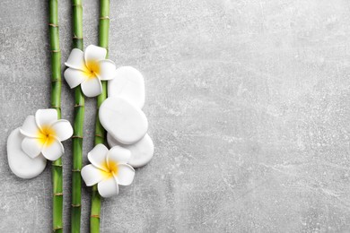 Spa stones, plumeria flowers and bamboo stems on light grey table, flat lay. Space for text