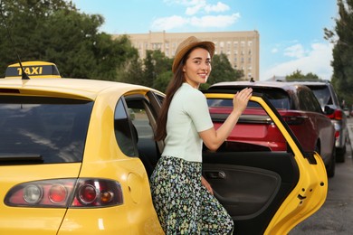 Photo of Beautiful young woman getting out of taxi on city street