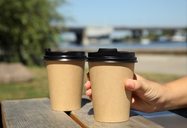 Woman taking cardboard coffee cup with plastic lid at wooden table outdoors, closeup