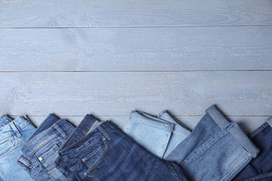 Collection of stylish jeans on grey wooden background, flat lay. Space for text