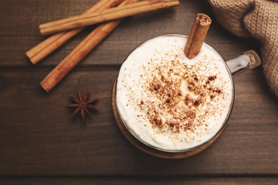 Cup of hot drink with whipped cream and aromatic cinnamon on wooden table, flat lay