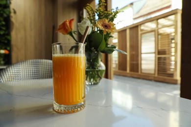 Glass of fresh orange juice on white table in cafeteria