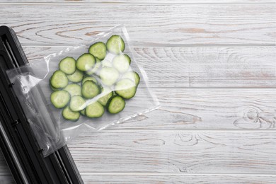 Vacuum packing sealer with plastic bag of cucumbers on white wooden table, flat lay. Space for text