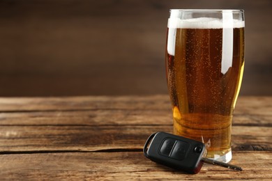 Car key near glass of alcoholic beer on wooden table, space for text. Dangerous drinking and driving