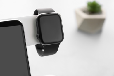 Stylish smart watch and phone charging with wireless pad against blurred background, closeup. Space for text