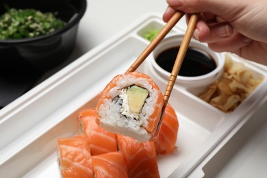 Photo of Woman eating sushi rolls with chopsticks at white table, closeup