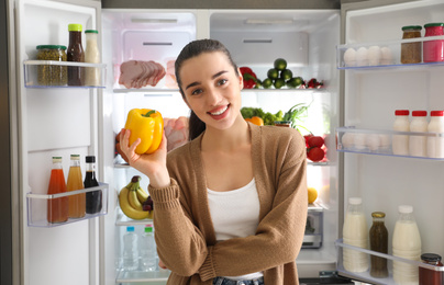 Young woman with bell pepper near open refrigerator