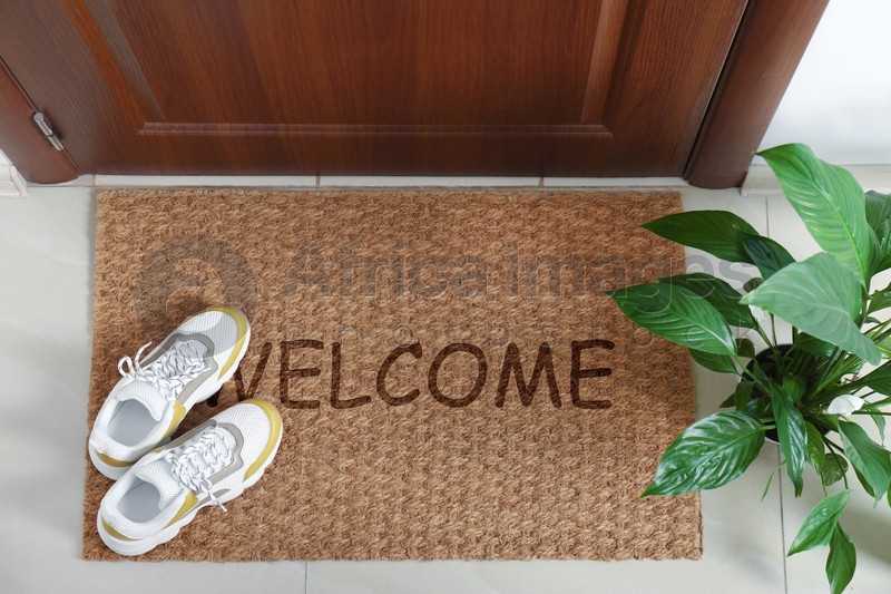 Door mat with word WELCOME and shoes near entrance, top view