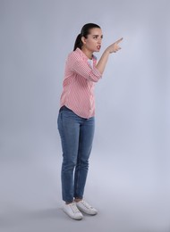 Emotional woman pointing with index finger on light grey background
