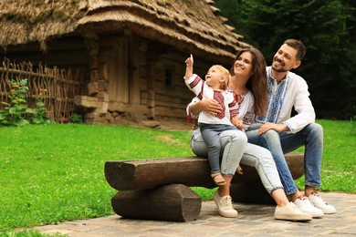 Happy family in Ukrainian national clothes sitting on bench outdoors