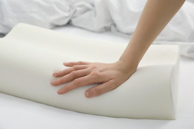 Photo of Woman touching orthopedic memory foam pillow on bed, closeup. Space for text