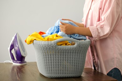 Photo of Woman with basket full of clean laundry at wooden table indoors, closeup