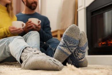 Photo of Lovely couple with hot drinks spending time together near fireplace at home, closeup