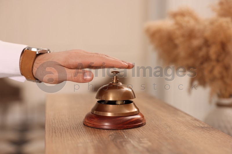 Photo of Man ringing service bell at wooden reception desk in hotel, closeup