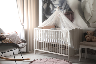 Baby room interior with stylish crib and floral wallpaper