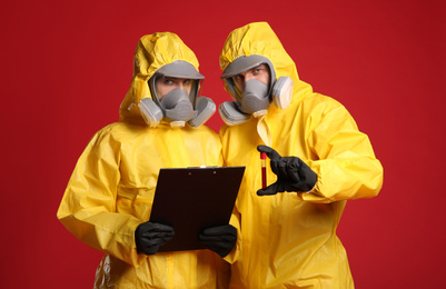 People in chemical protective suits with blood sample and clipboard on red background. Virus research